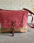Two-toned red and brown bag with leather strap on a concrete floor against a white brick wall.
